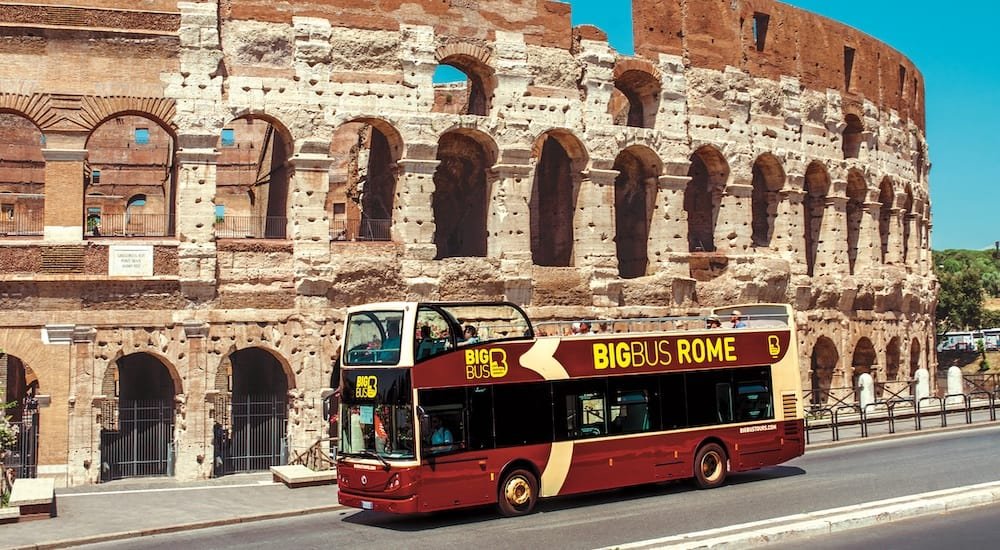 A hop-on hop-off bus driving past the Colosseum